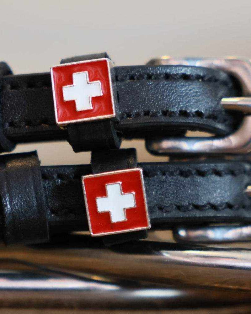 Close-up of red Swiss-flag charms with white cross on black leather spur straps