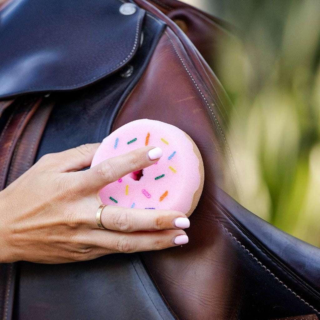 Hand holding pink donut-shaped tack sponge cleaning a brown leather equestrian saddle from Donutz Equestrian Bundle