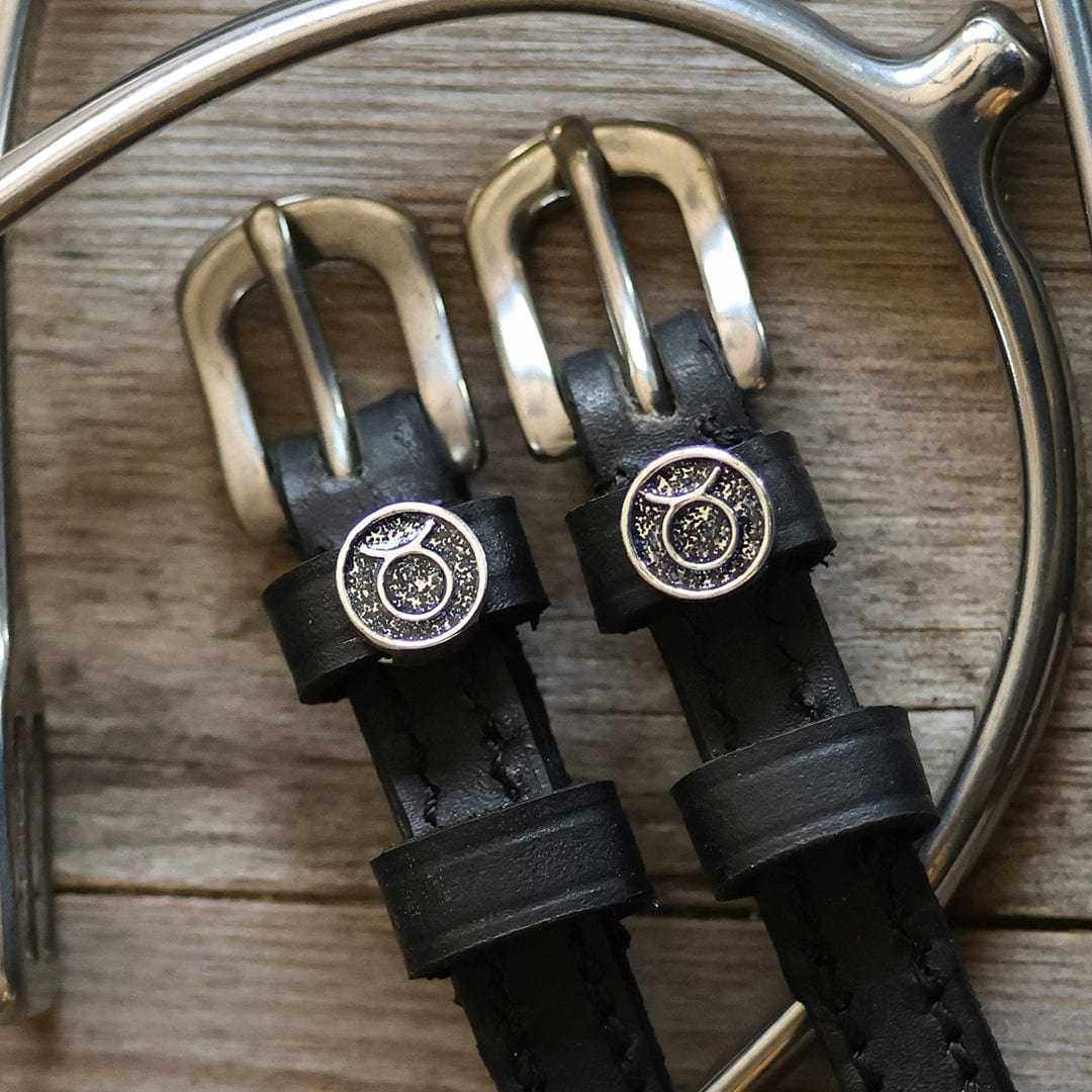 Close-up of Taurus zodiac charms and brass buckles on black leather spur straps
