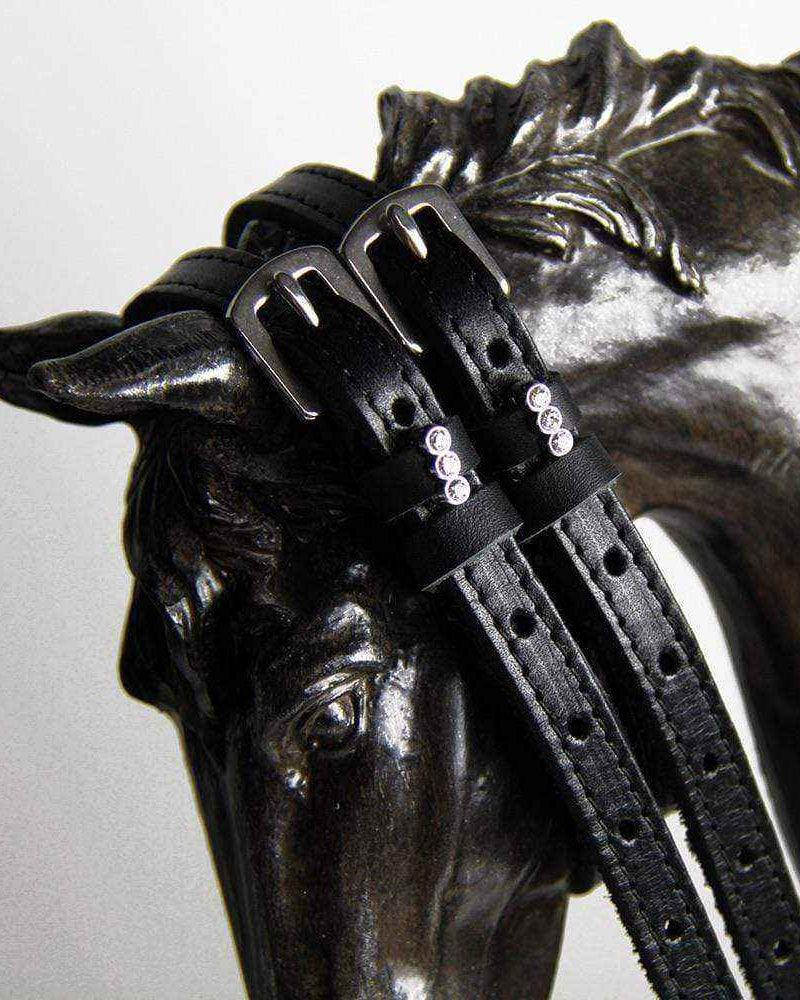 Black crystal-charm spur straps draped over a bronze horse-head sculpture
