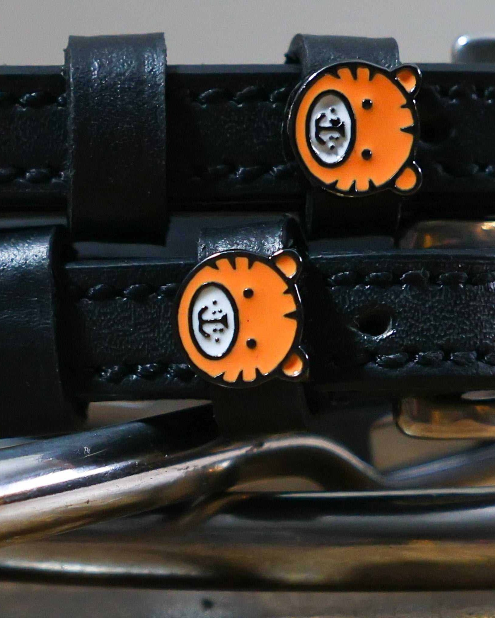 Close-up of orange tiger-face charms on black leather spur strap keepers