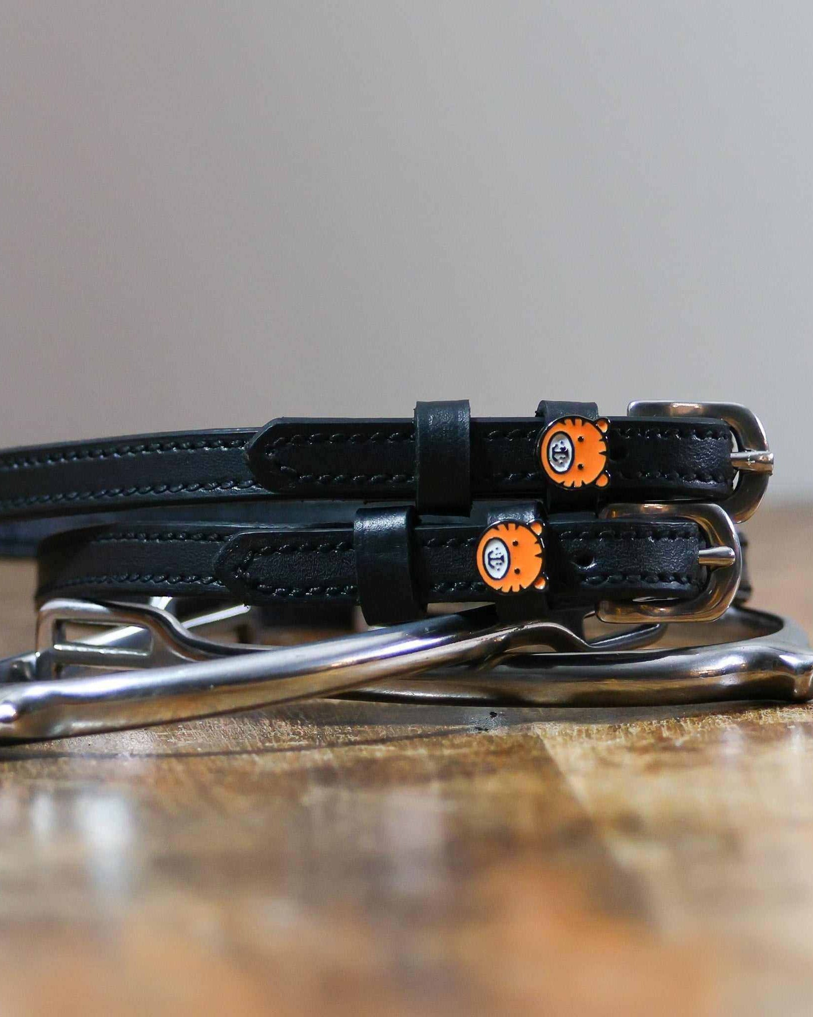 Black tiger spur straps coiled on a silver stirrup on a wooden table