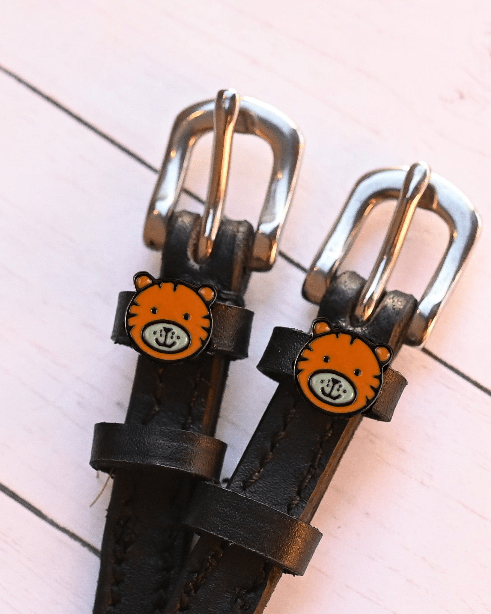 Tiger-face charm spur straps with silver buckles on pink-painted wood planks