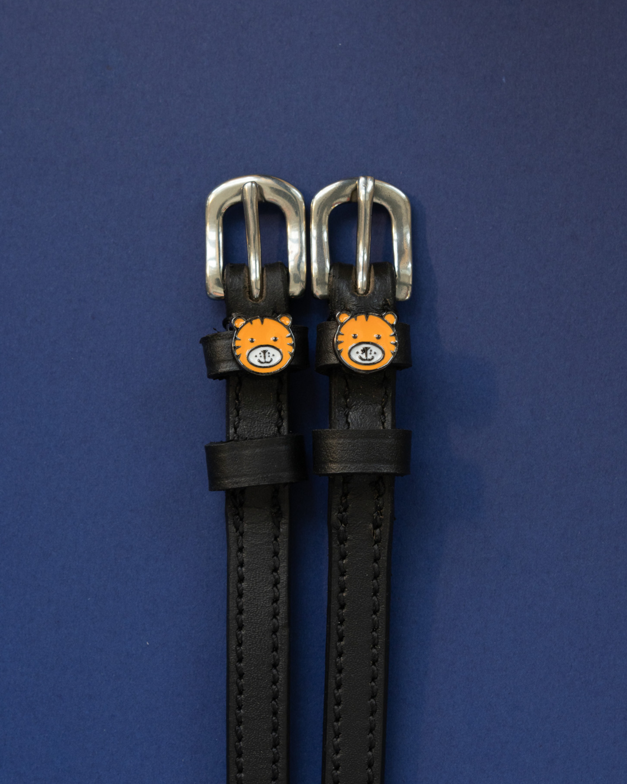 ManeJane tiger spur straps with silver buckles laid flat on navy blue
