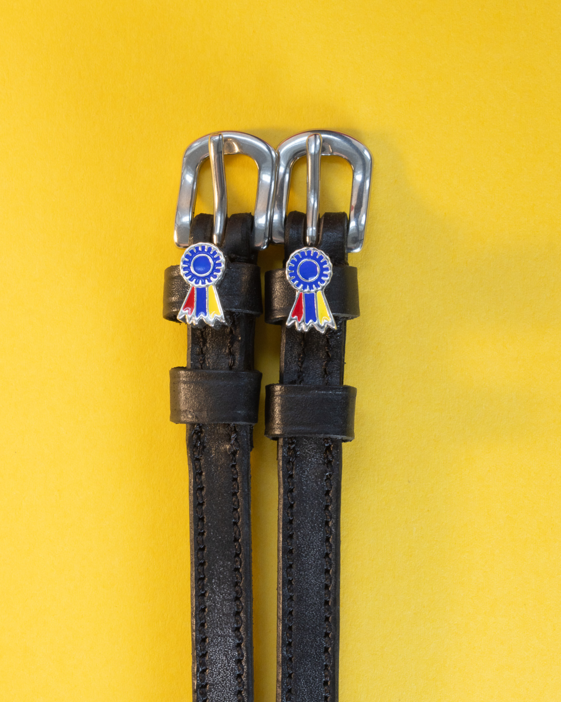 Black leather spur straps with blue and tri-color ribbon rosette charms on yellow
