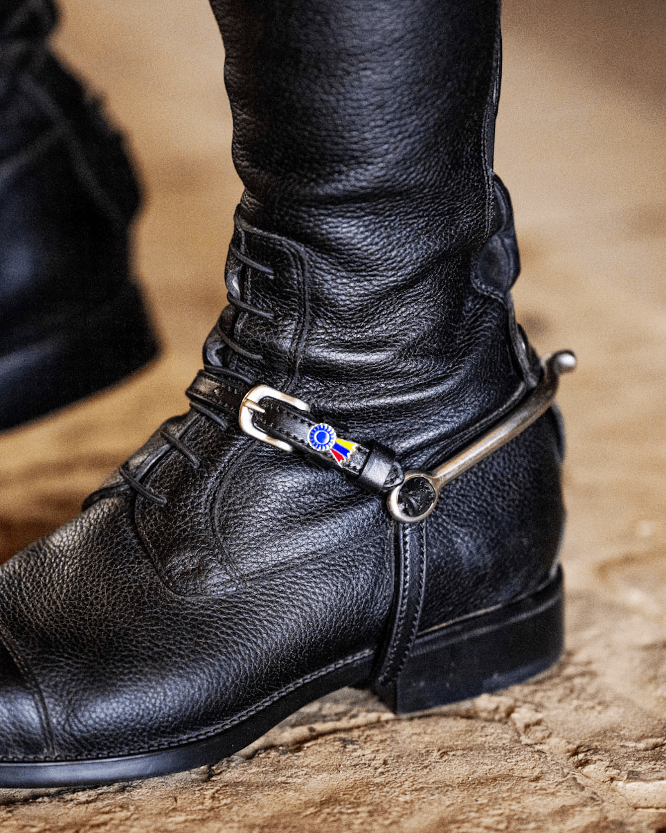 Tri-color ribbon spur strap fastened on a rider's black English riding boot with spur
