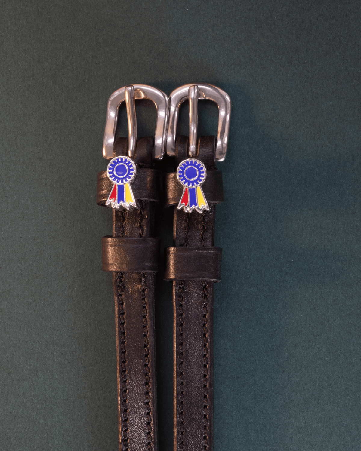 Pair of black leather rosette spur straps flat-laid on a dark green background