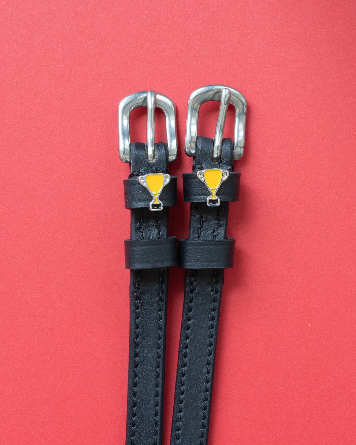 Trophy ManeJane spur straps with the signature Trophy charm, shown on a coral background