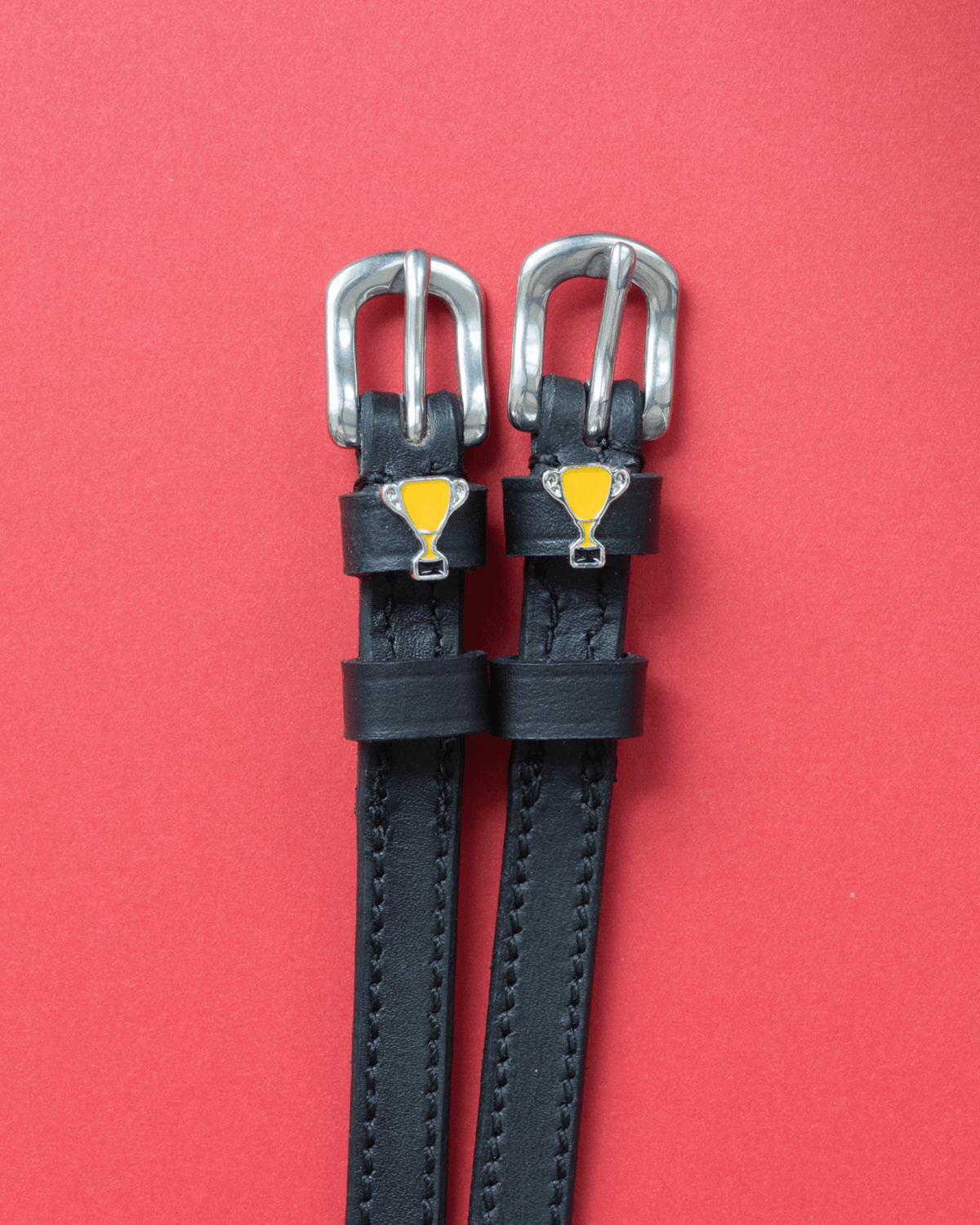 Trophy ManeJane spur straps with the signature Trophy charm, shown on a coral background