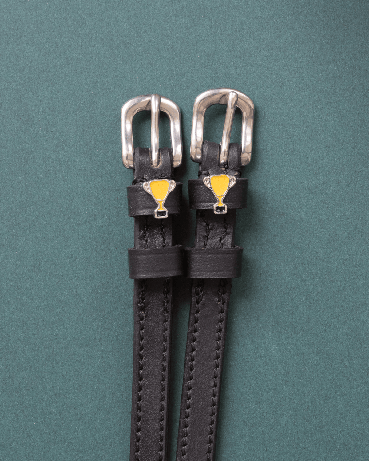 Trophy ManeJane spur straps with the signature Trophy charm, shown on a green background, by Dreamers & Schemers