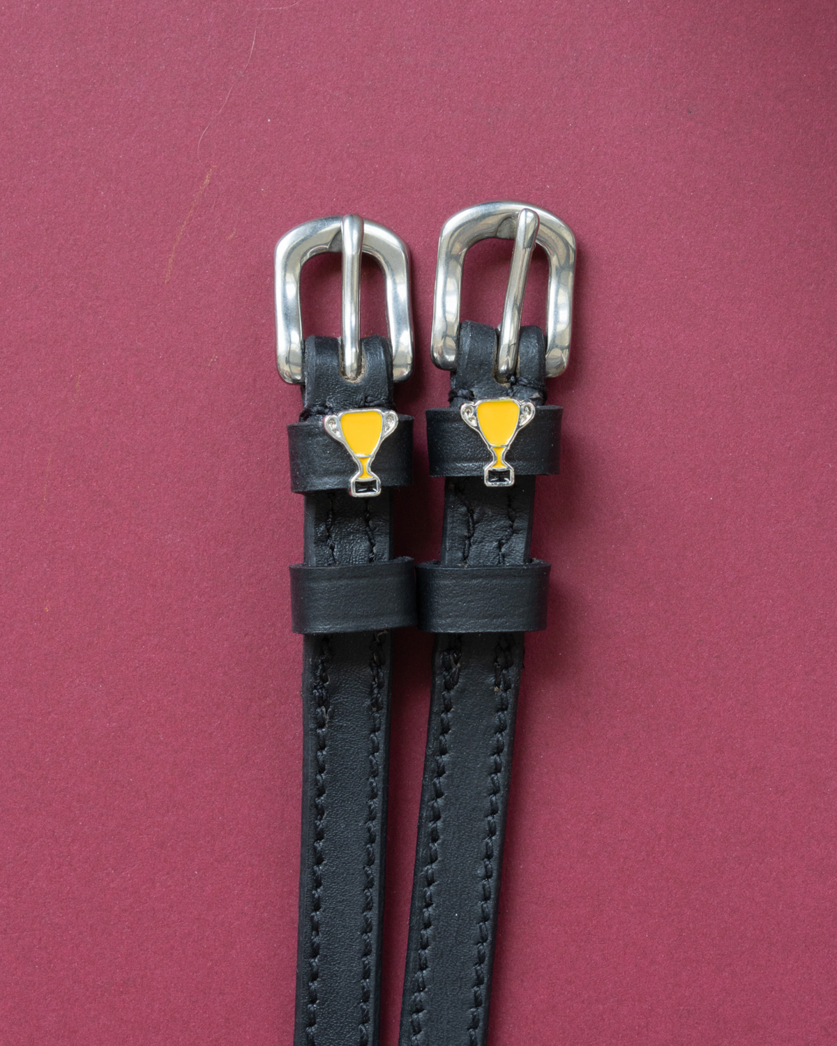 Trophy ManeJane spur straps with the signature Trophy charm, shown on a red background
