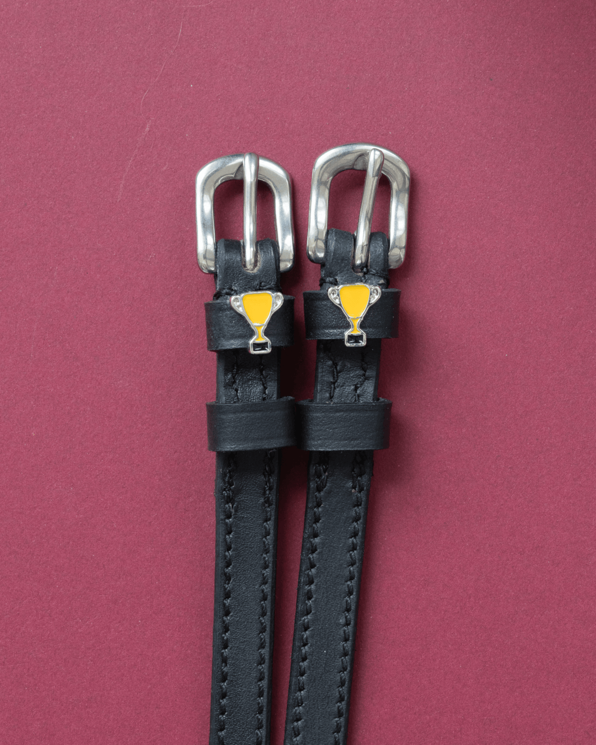 Trophy ManeJane spur straps with the signature Trophy charm, shown on a red background