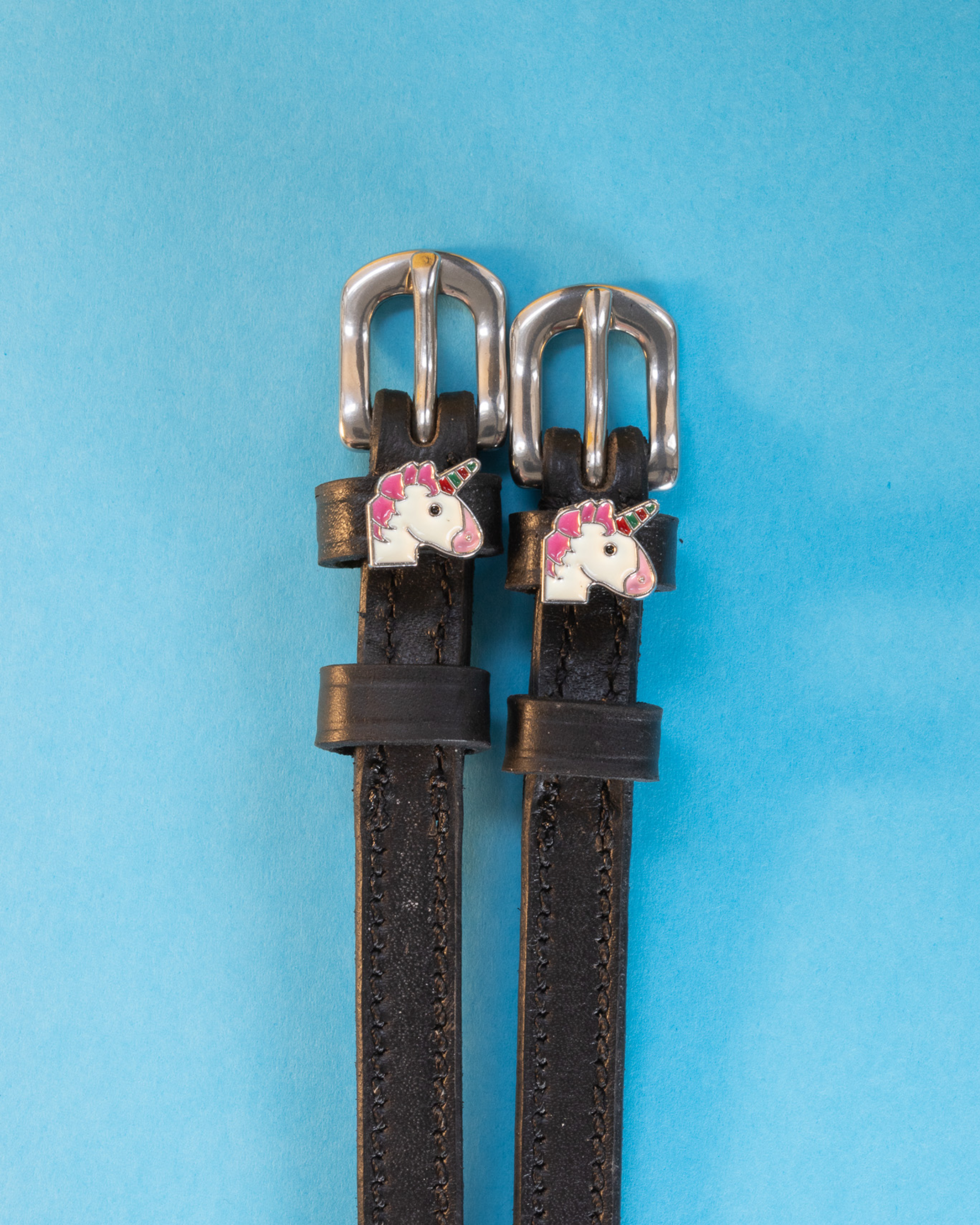 ManeJane unicorn spur straps with silver buckles flat-laid on a bright blue background