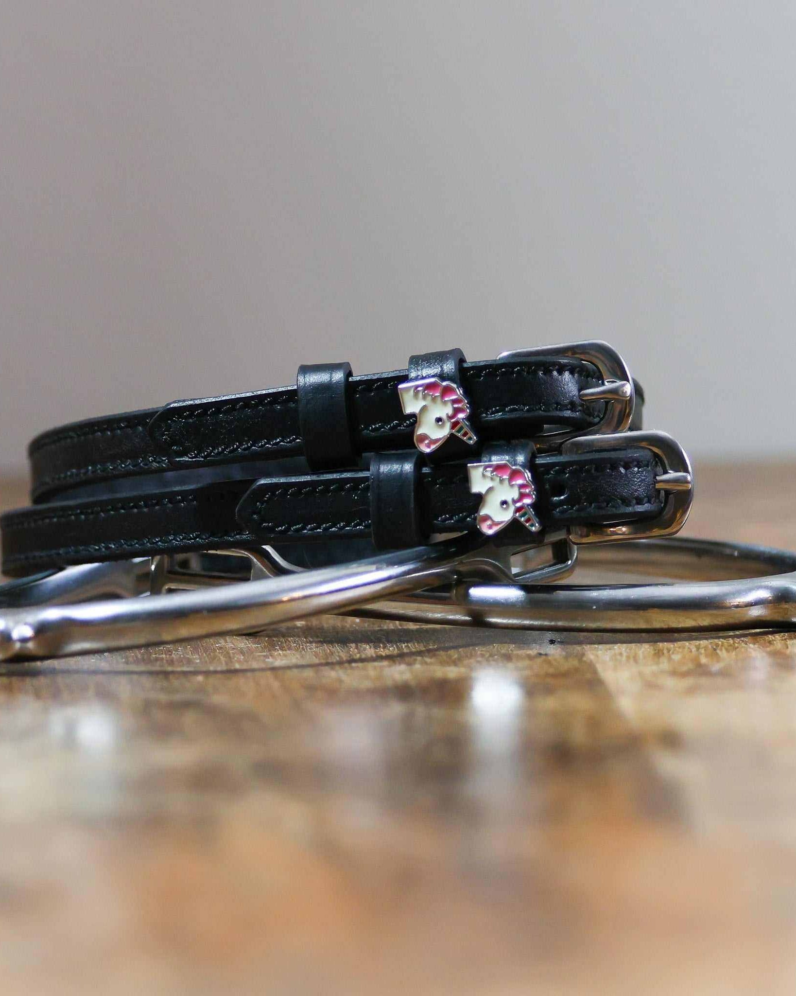 ManeJane unicorn spur straps coiled beside a silver stirrup on a wooden tabletop