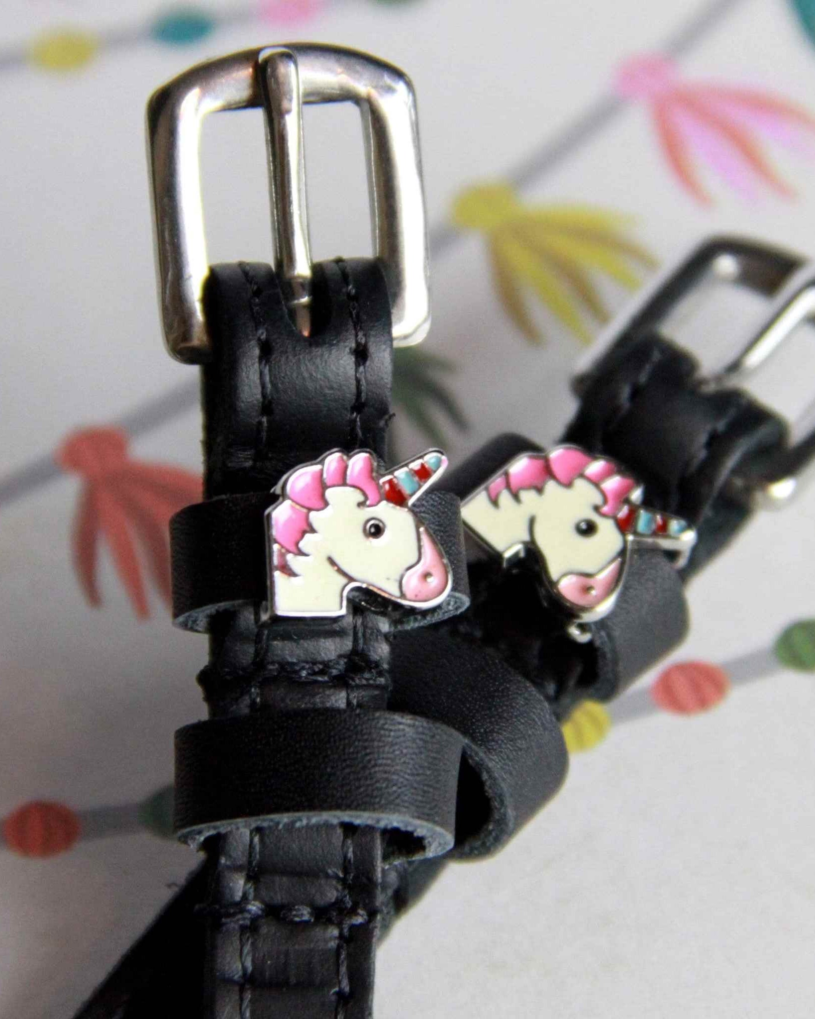 Angled view of unicorn charm ManeJane spur straps on a colorful party-streamer backdrop