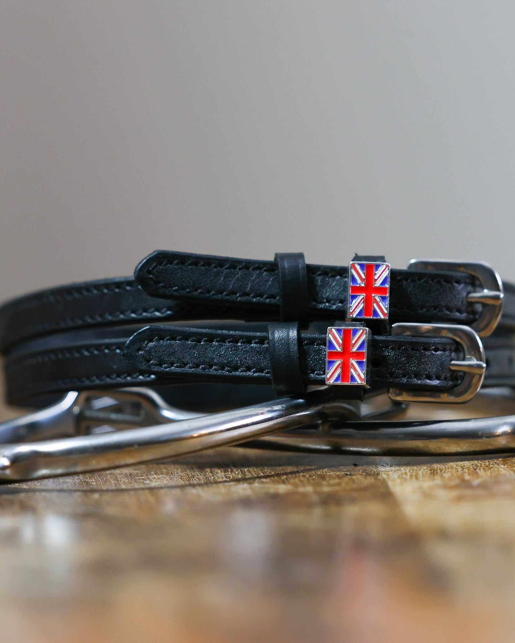 Coiled black leather Union Jack flag spur straps stacked on a silver spur on wood