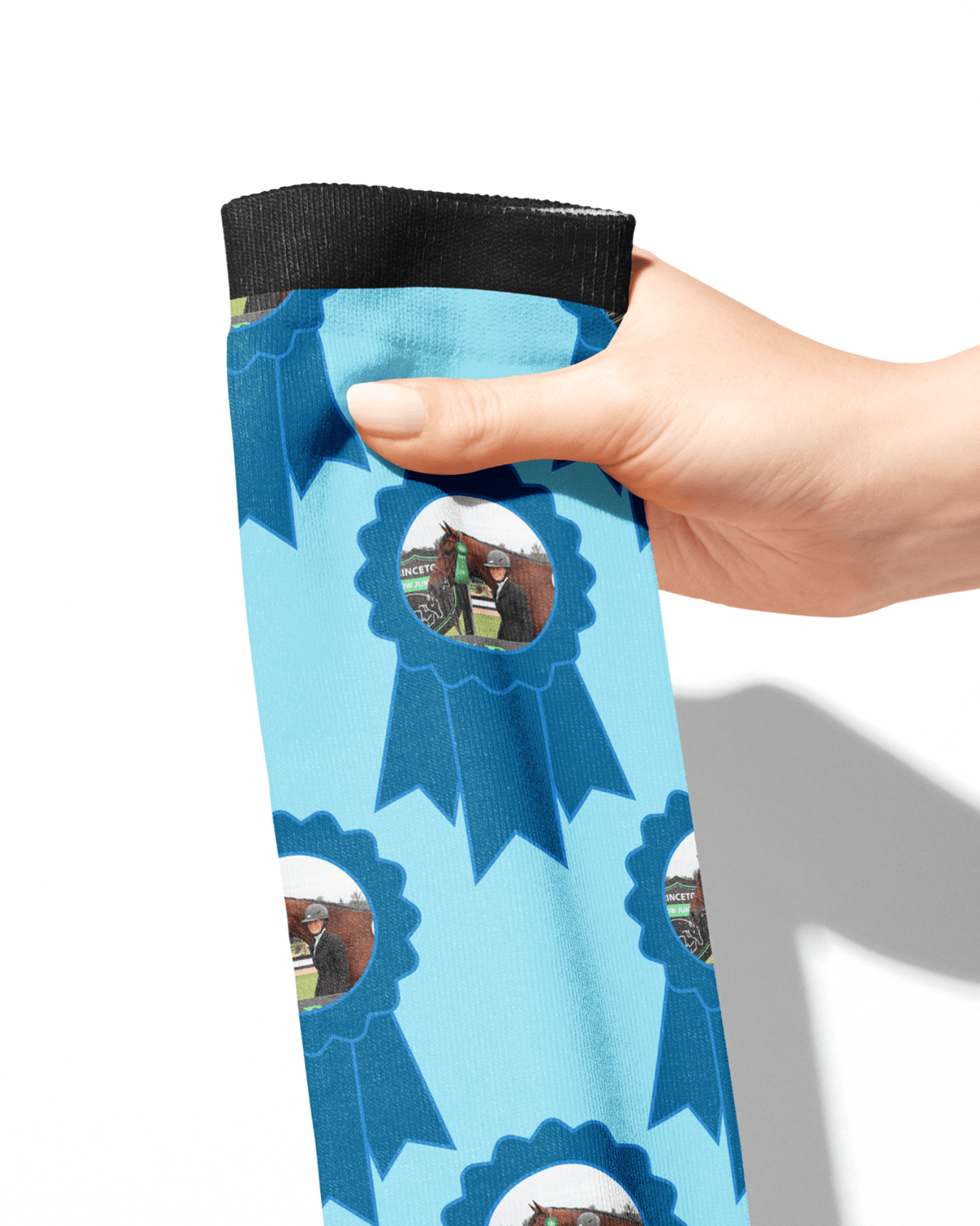 Hand holding custom blue ribbon socks with personalized photo of horse against white background