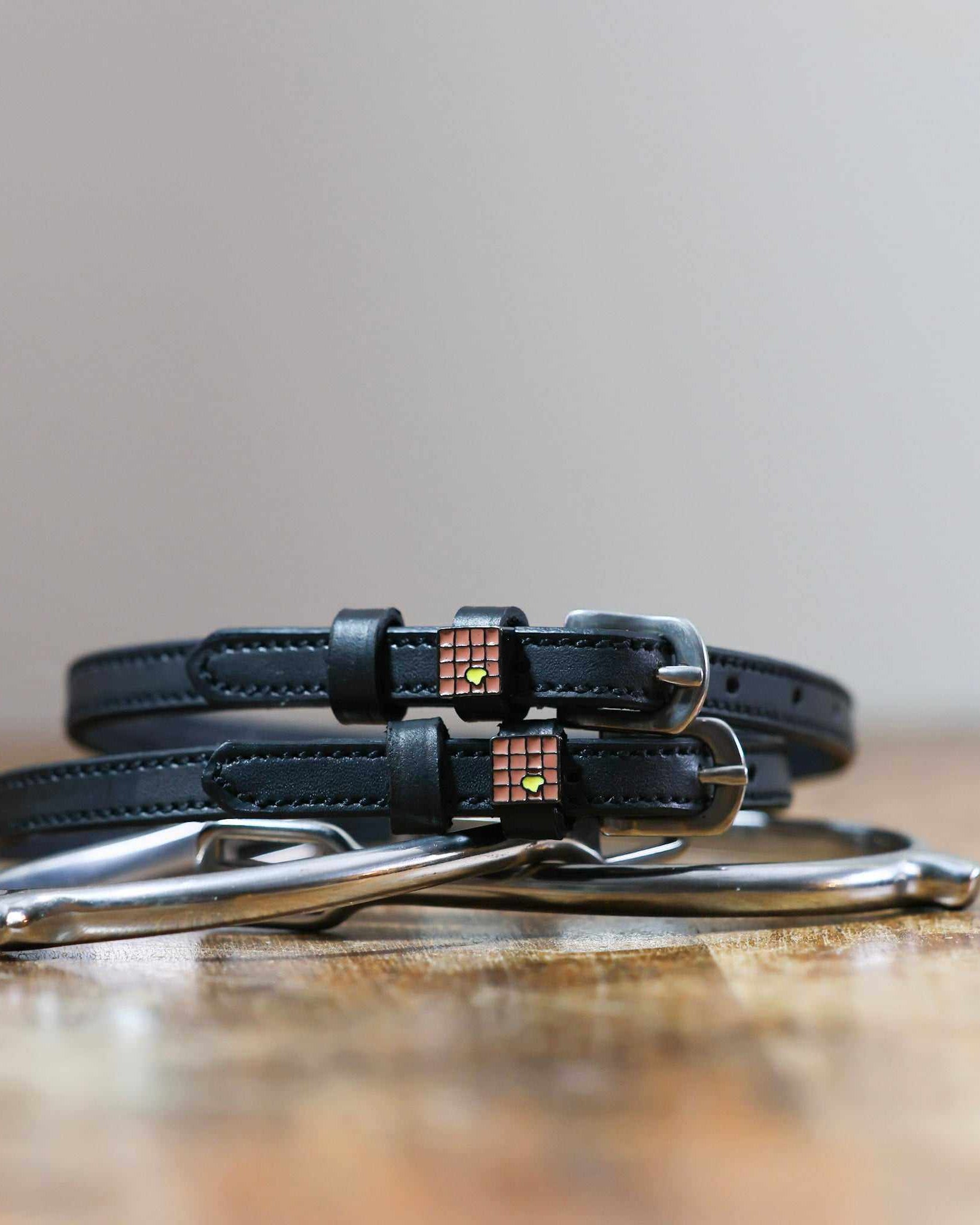 Black leather waffle spur straps coiled on wood beside a stirrup