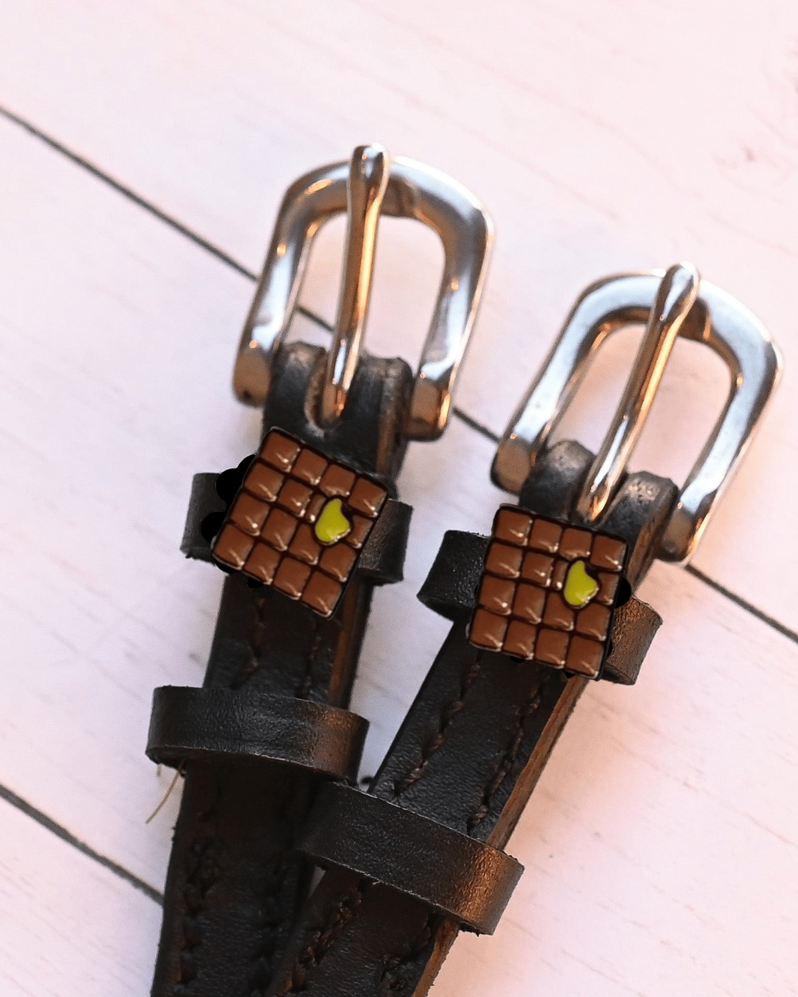 Angled close-up of waffle-and-butter spur strap charms on pale pink planks