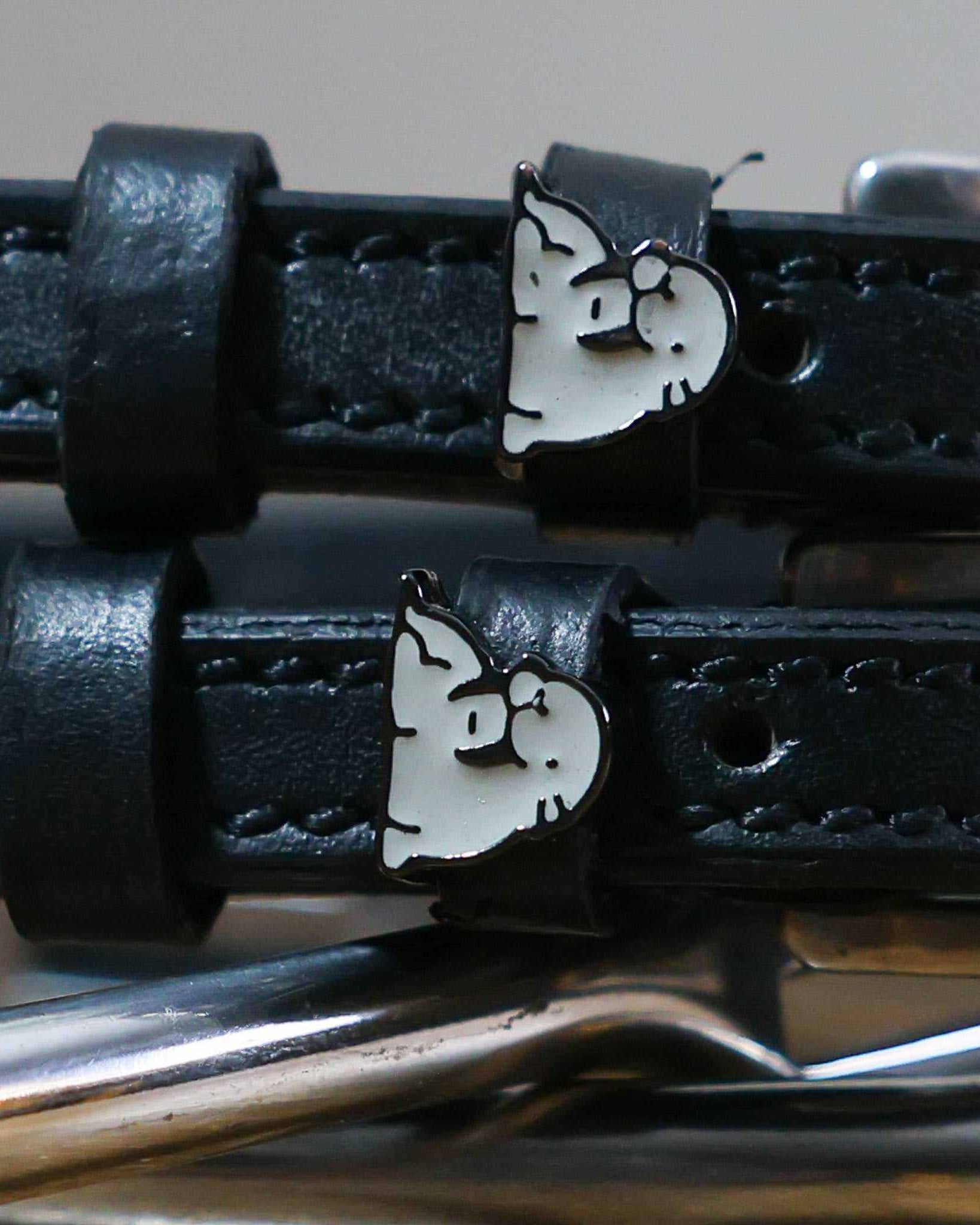 Black leather ManeJane spur straps with silver buckles and grey walrus charms on royal blue