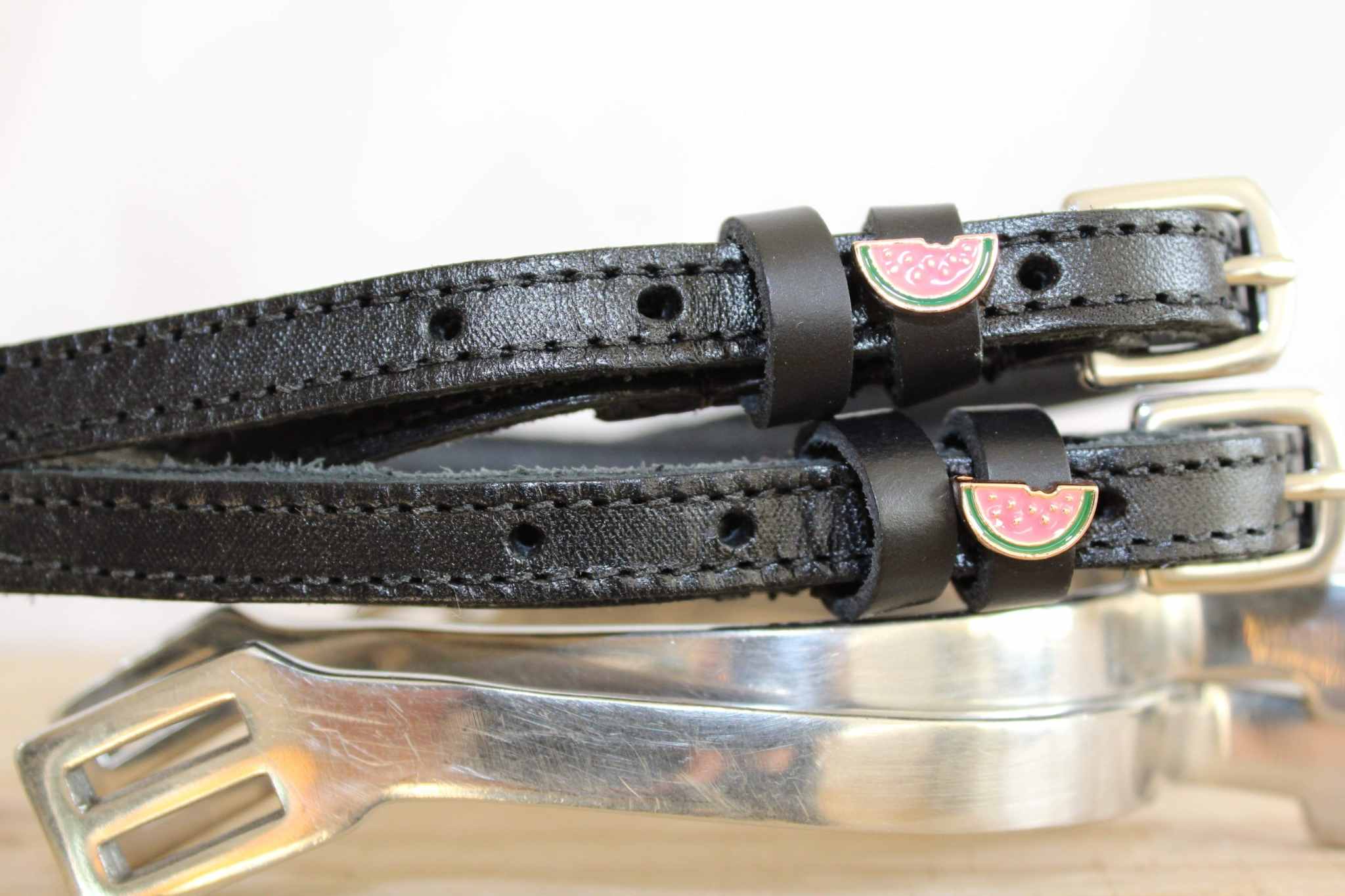 Brown leather ManeJane watermelon spur straps with rose-gold buckles on pale blue