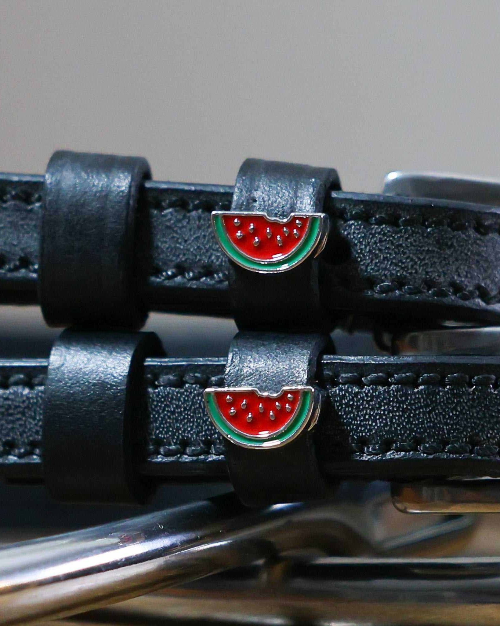 Close-up of enamel watermelon slice charms on black leather ManeJane spur strap keepers