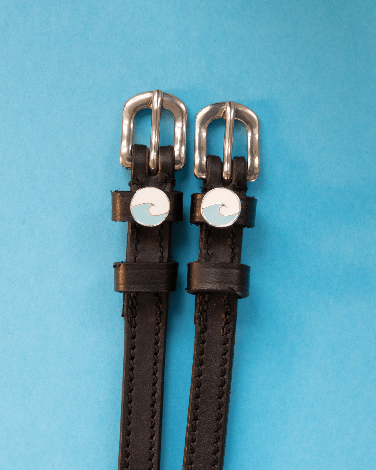 Black leather ocean wave spur straps on a light blue background