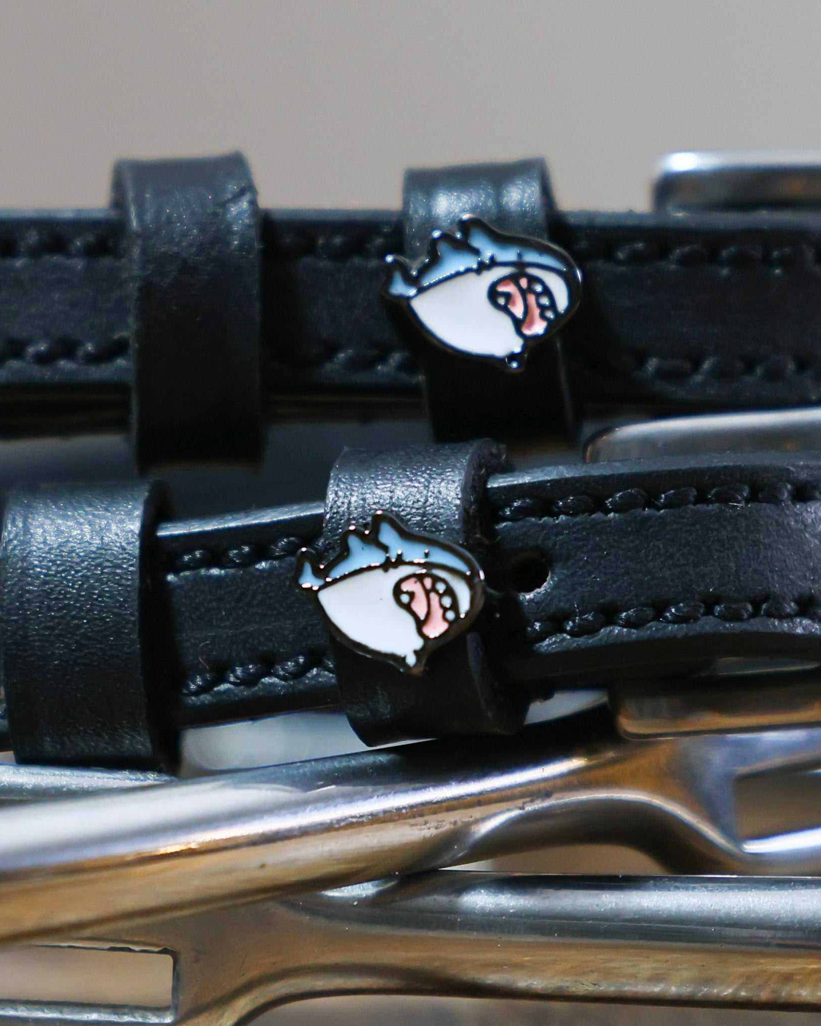Close-up of a blue-and-white shark head charm on a black leather ManeJane spur strap keeper