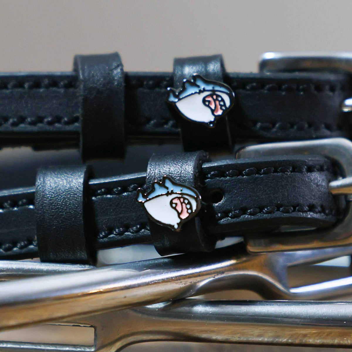 Close-up of a blue-and-white shark head charm on a black leather ManeJane spur strap keeper