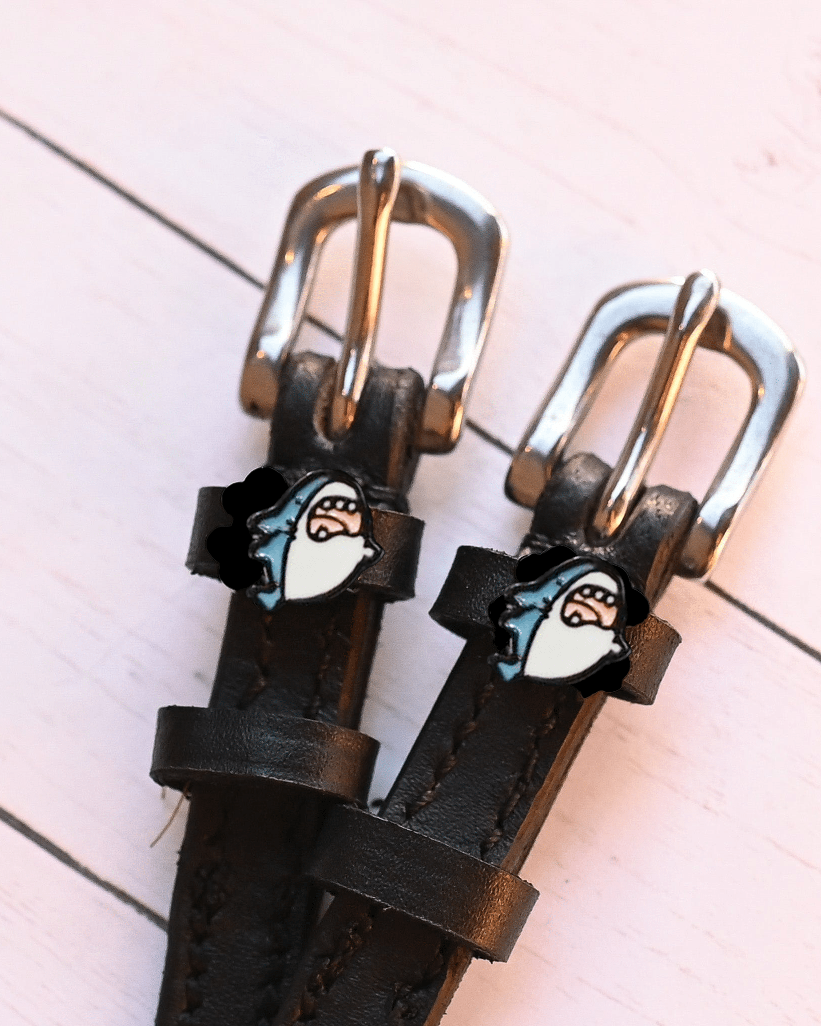 Silver buckles and shark head charms of black leather spur straps on pink painted wood