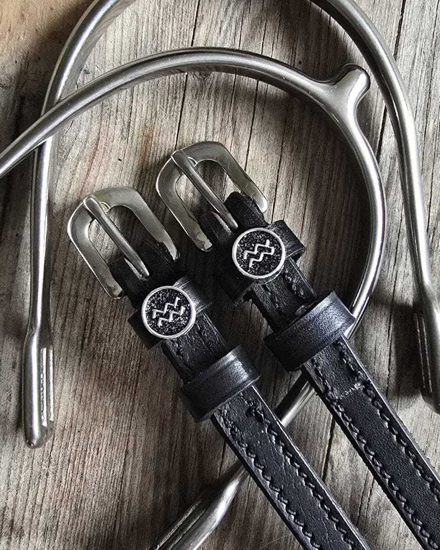 Black leather Aquarius Spur Straps with stainless steel buckles and custom charm on wooden background