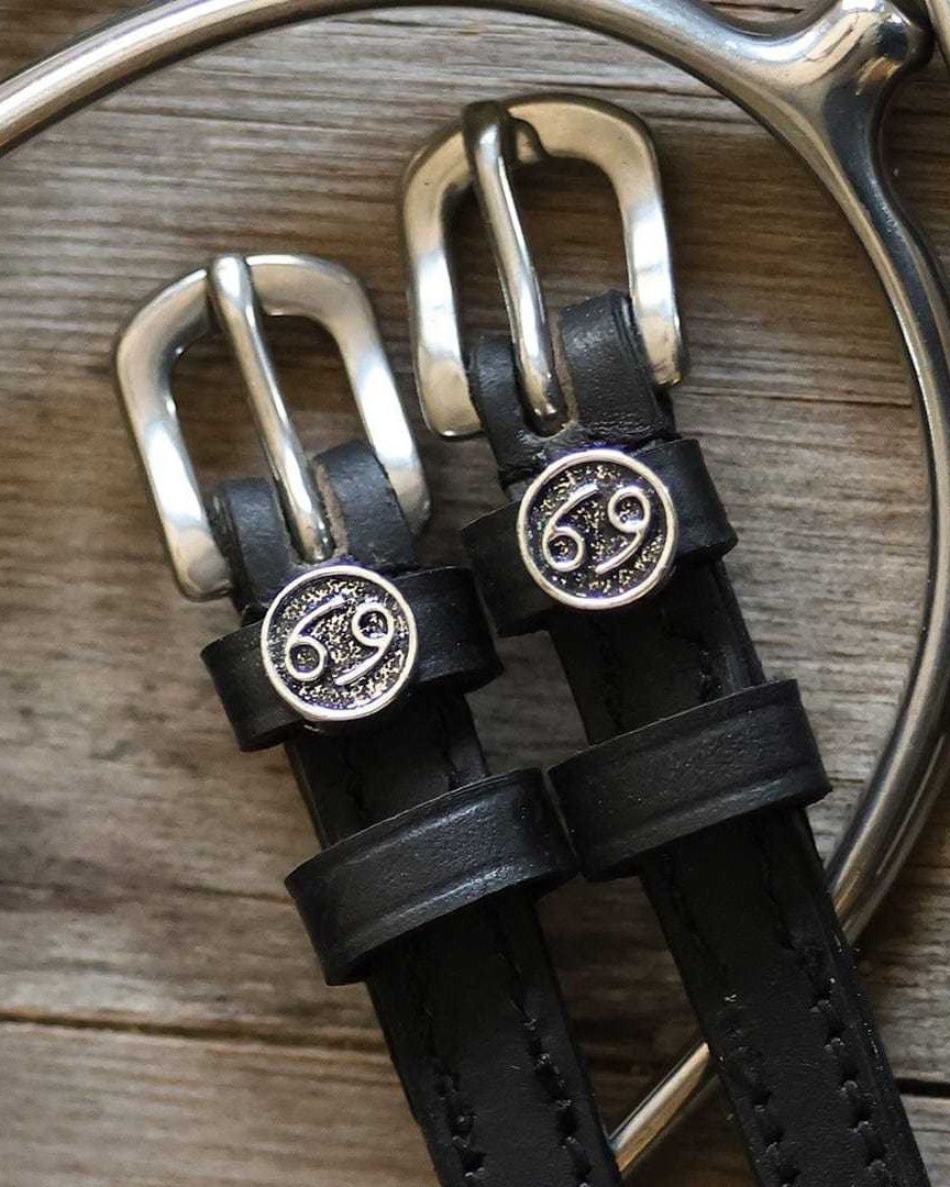 Black leather Cancer Spur Straps with stainless steel buckles and custom Cancer zodiac charms on wooden background