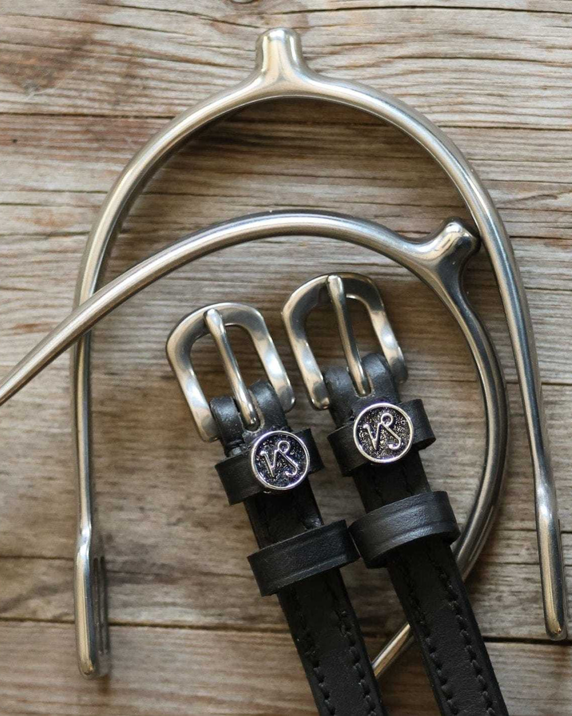 Capricorn Spur Straps black leather with stainless steel buckles and custom charm on wooden background