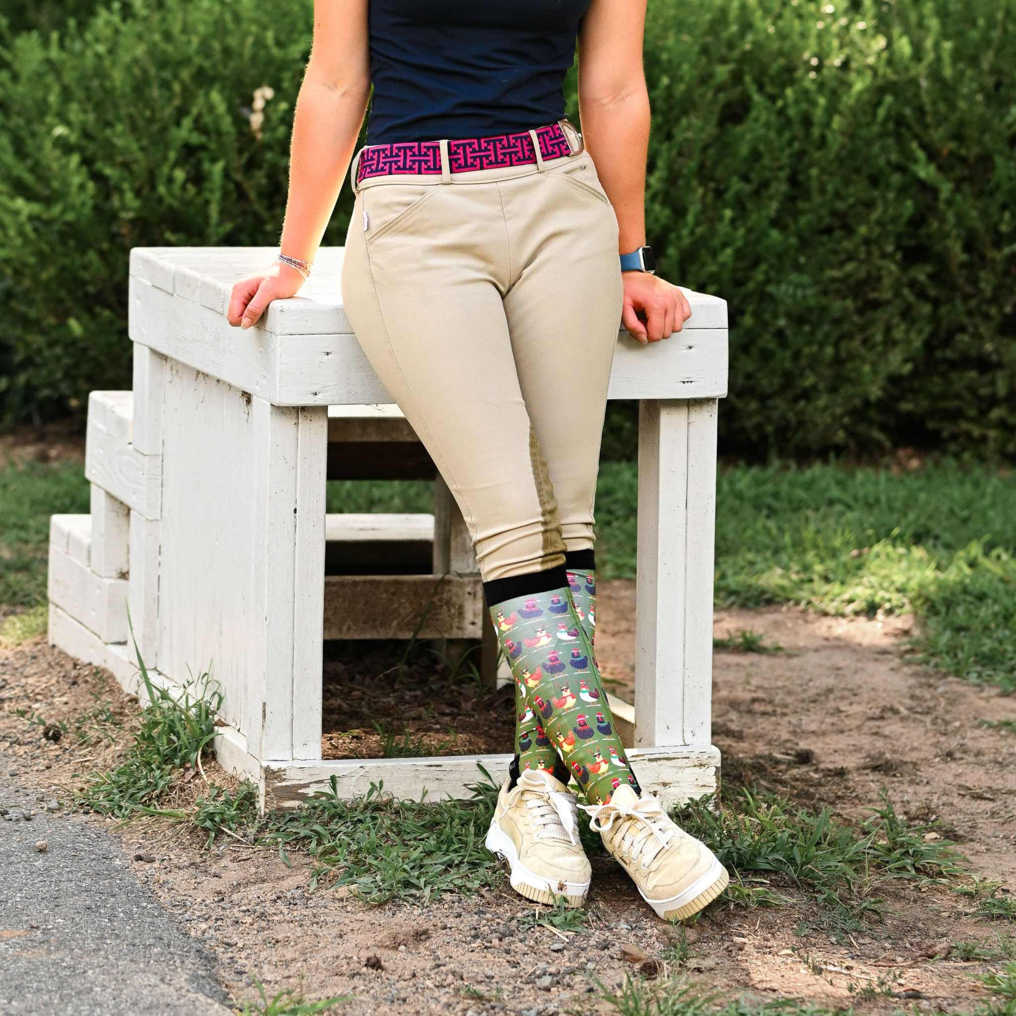Person wearing colorful Cluck-Mas boot socks with black tops and beige riding pants outdoors