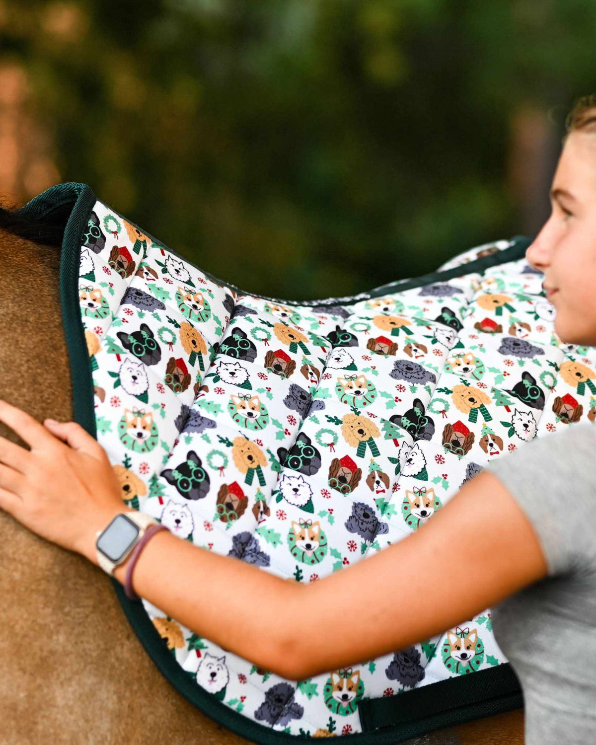 Deck the Paws Saddle Pad with colorful dog pattern on horse back, woman adjusting the pad