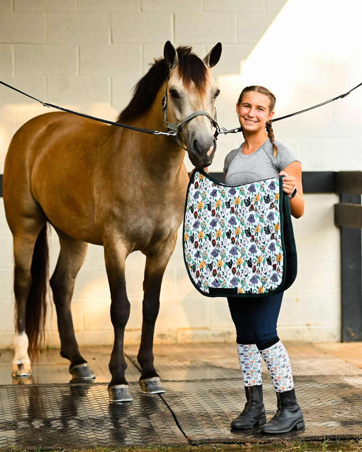 Woman holding Deck the Paws Saddle Pad next to brown horse in stable