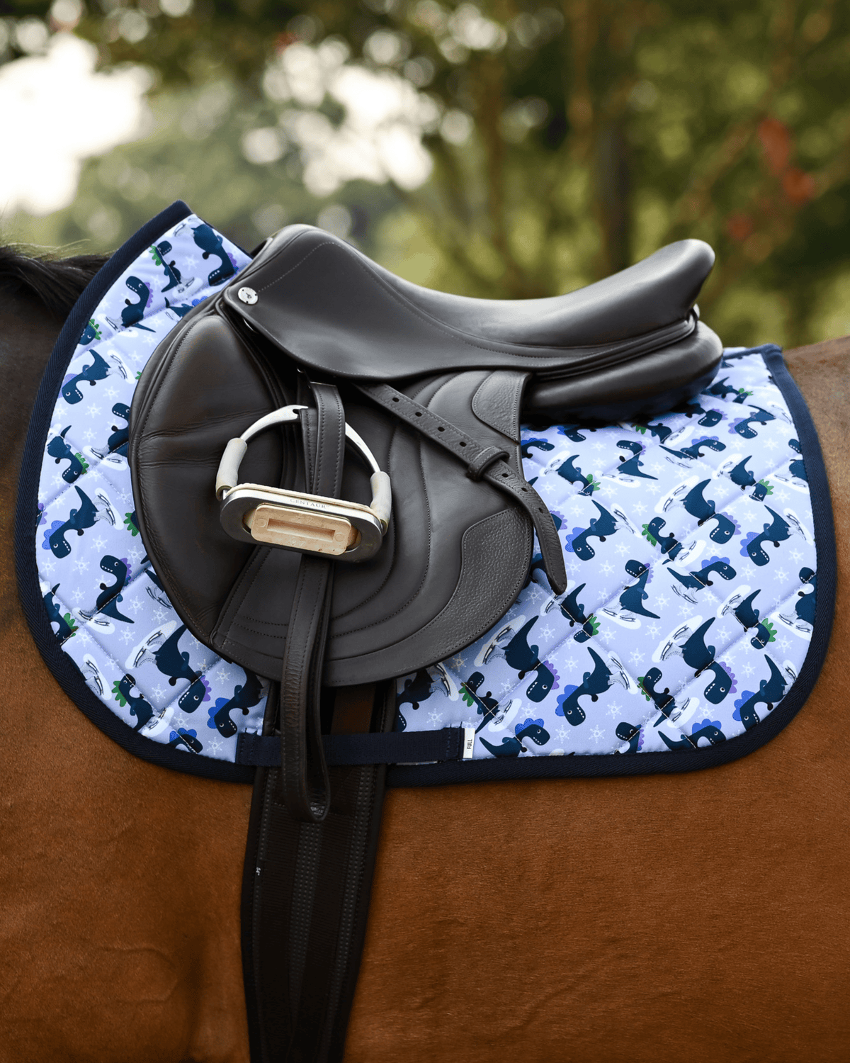 Side view of the Dino-skate saddle pad on a bay horse, tacked up with a brown jump saddle and stirrup down