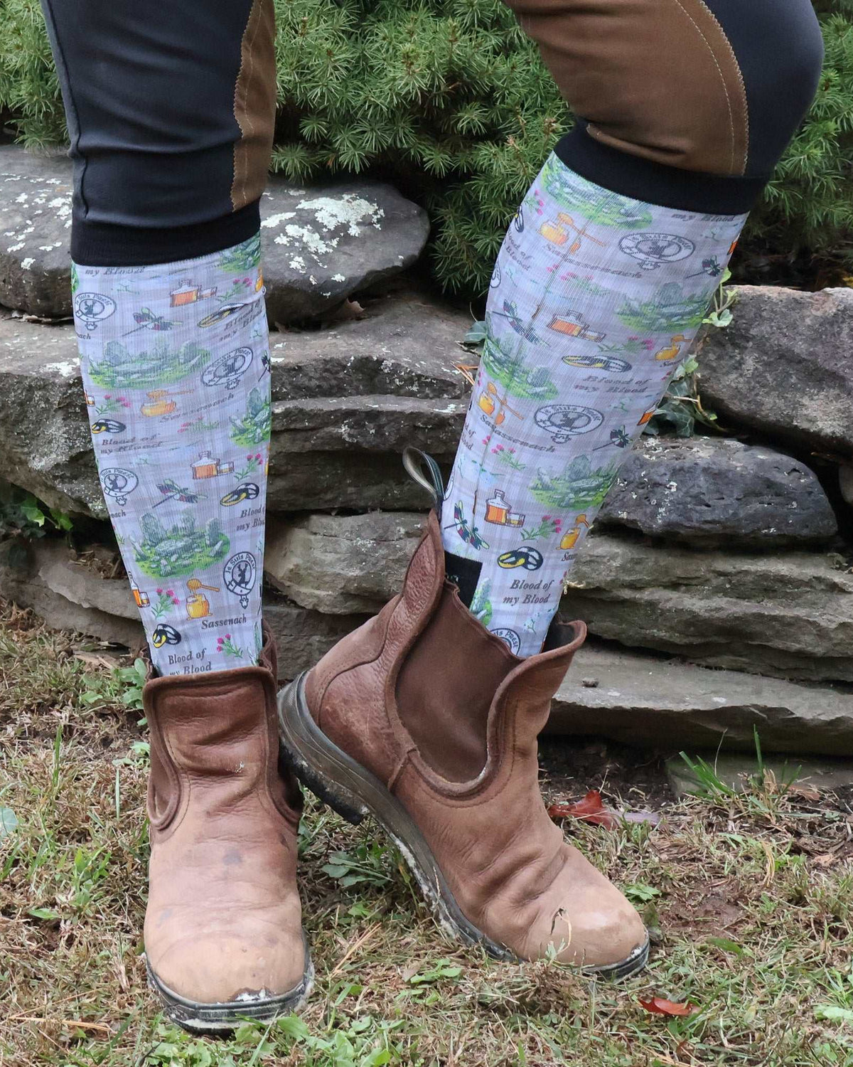 Limited edition Blood of My Blood boot socks with Outlander-inspired design worn with brown riding boots outdoors