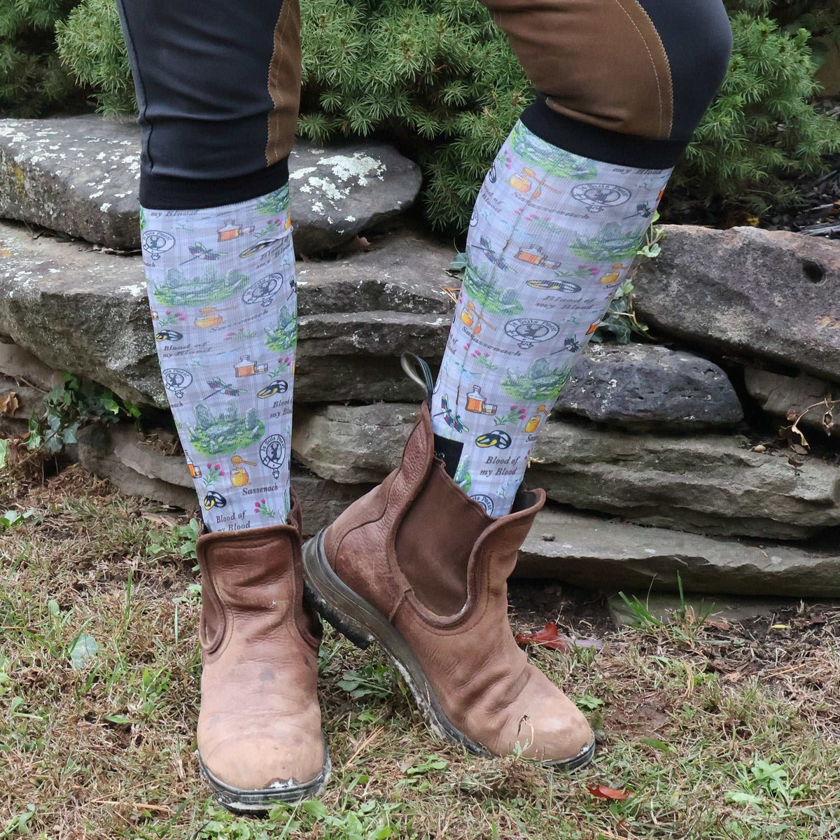 Limited edition Blood of My Blood boot socks with Outlander-inspired design worn with brown riding boots outdoors