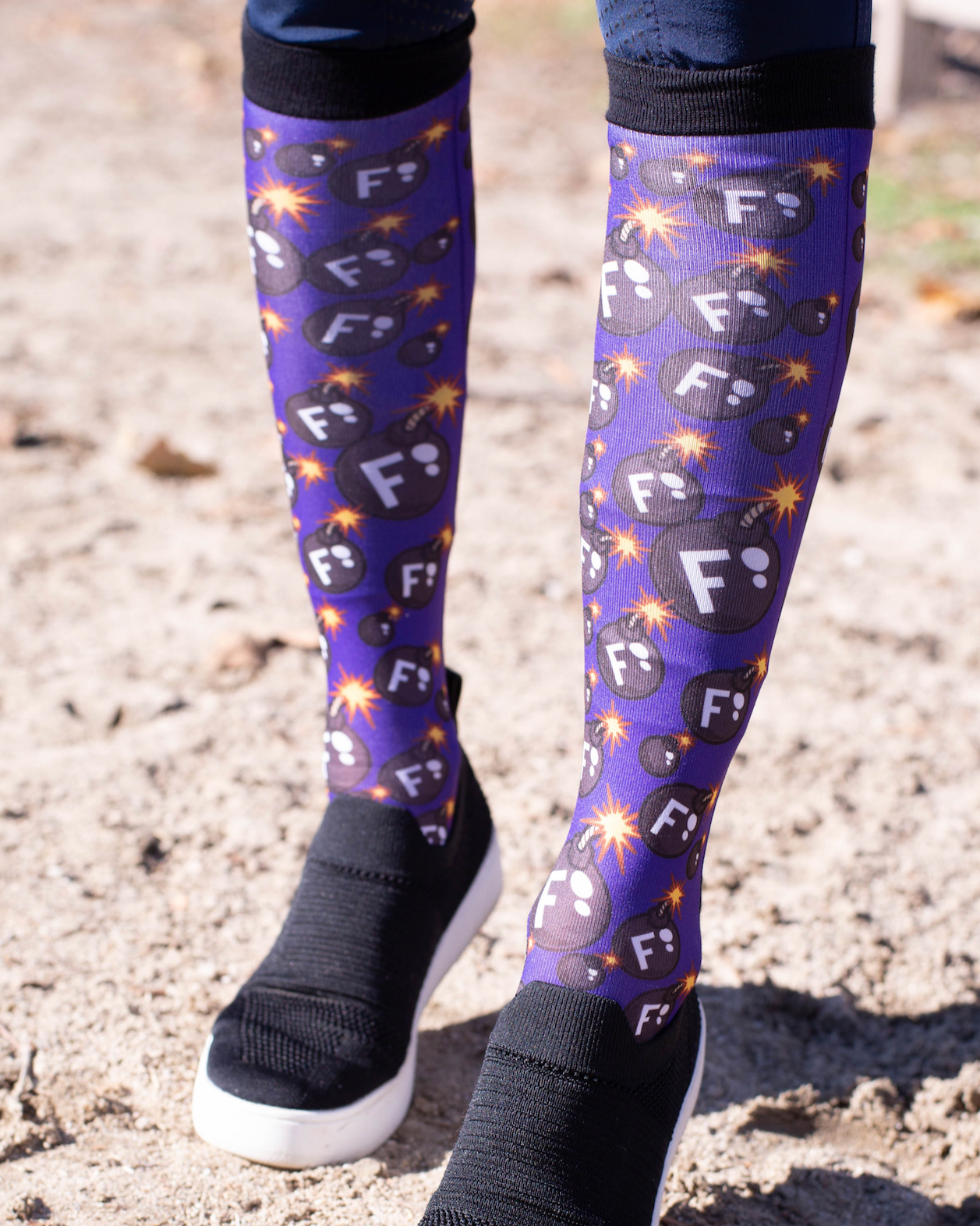 Ultimate F-Bomb Pack equestrian boot socks with bomb and F-letter design on rider's legs outdoors