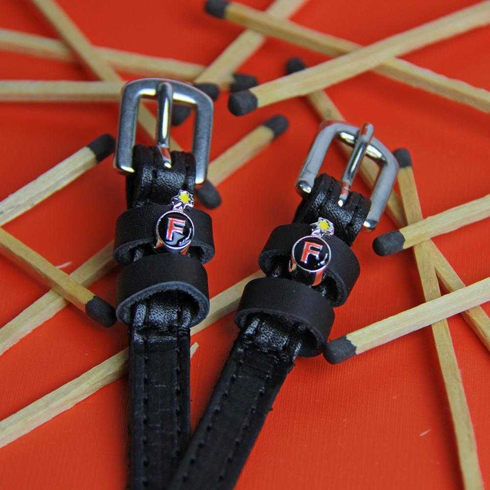 Close-up of PlainJane black leather spur straps with silver buckles from the Ultimate F-Bomb Pack on orange background with scattered matchsticks