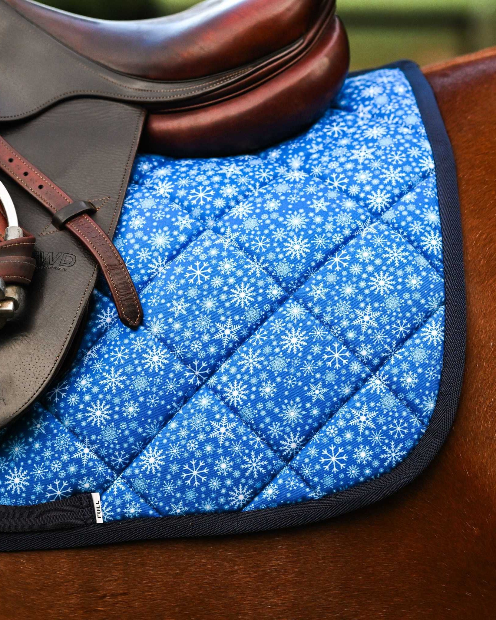 Blue Flake It til You Make It saddle pad with snowflake pattern under brown leather saddle on horse