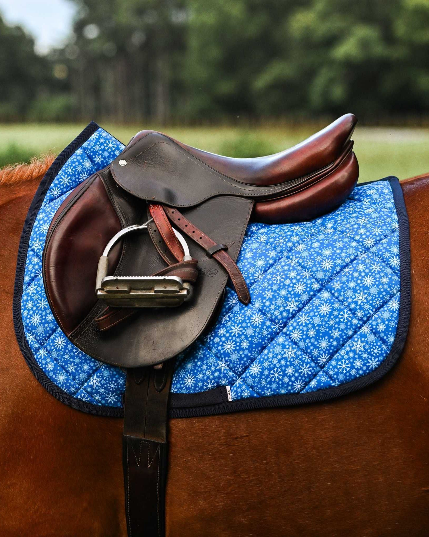 Blue Flake It til You Make It saddle pad with snowflake pattern under brown English saddle on horse