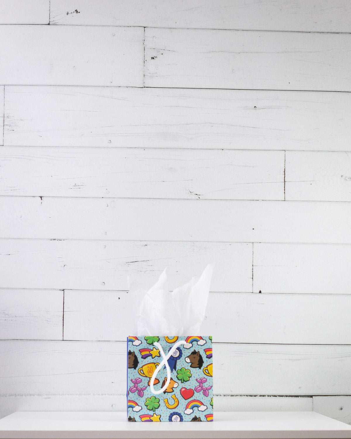 Full O' Luck small gift bag on a white shelf, aqua print of clovers, rainbows, horseshoes and hearts.