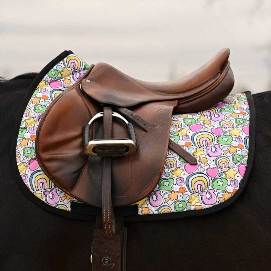 Brown leather saddle on horse with colorful Lucky Equestrian Bundle Full O’ Luck saddle pad featuring clovers, rainbows, and horseshoes