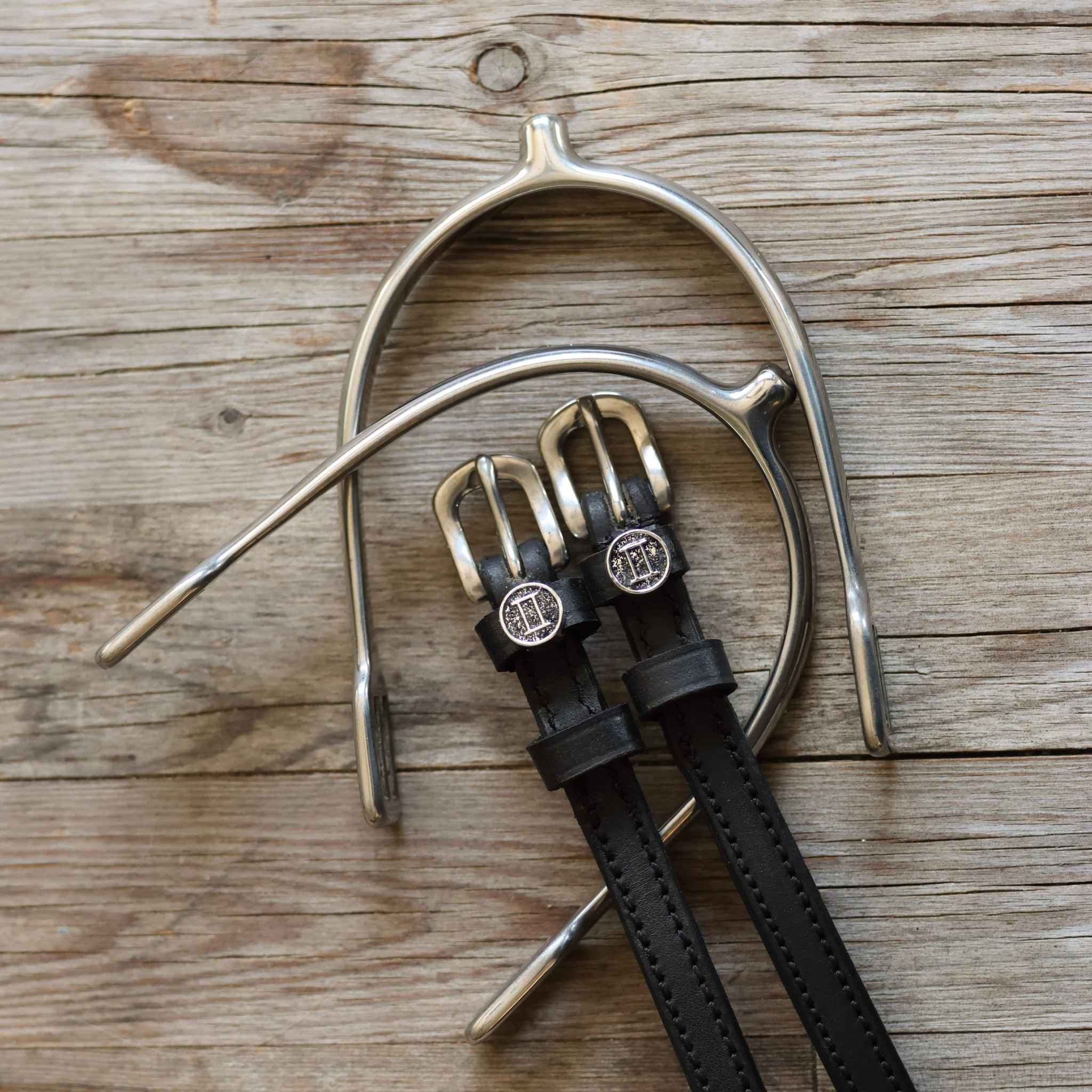 Gemini Spur Straps black leather with stainless steel buckles and custom charms on wooden background
