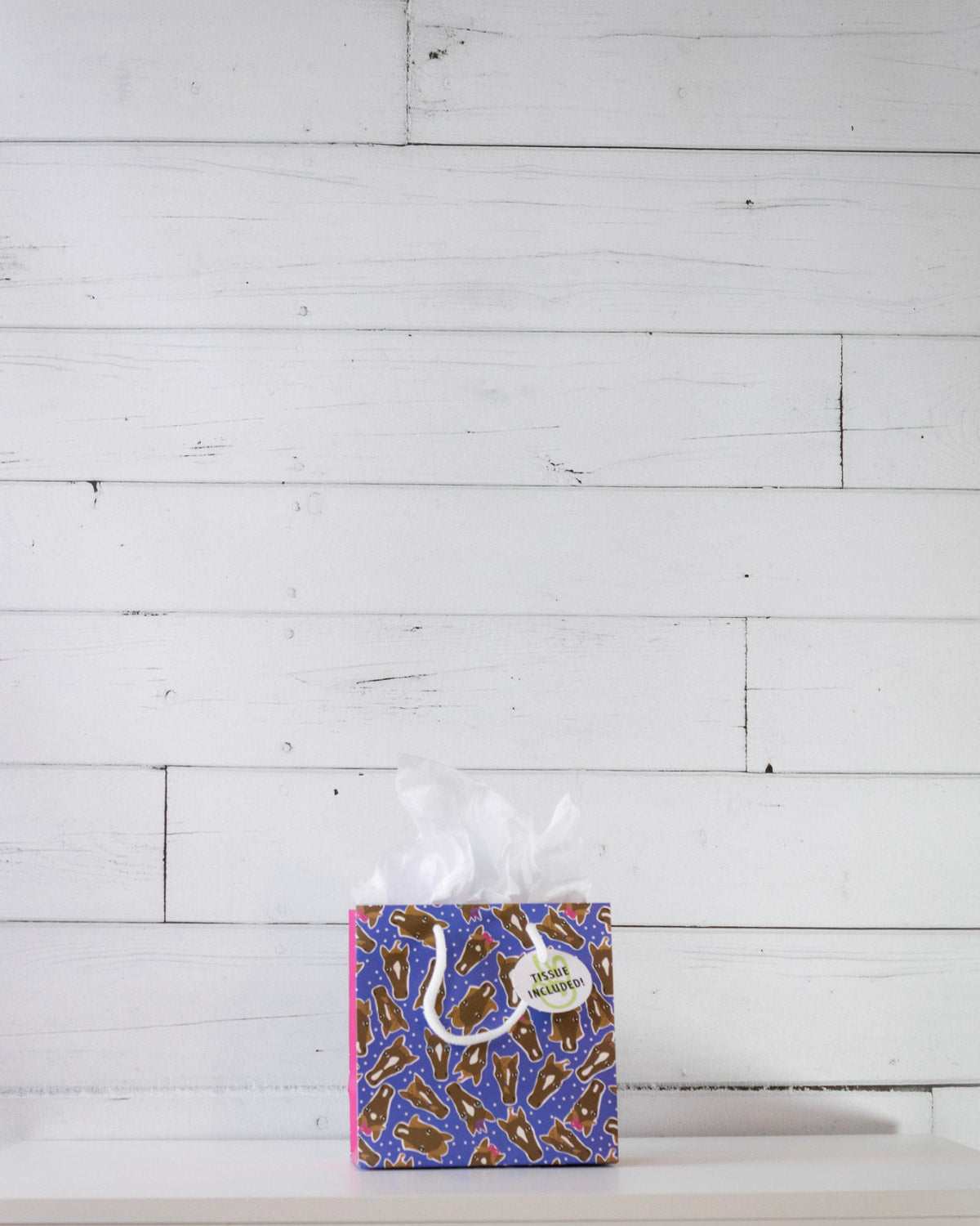Hairy Styles small gift bag on a white shelf, square blue panel scattered with cartoon pony faces.