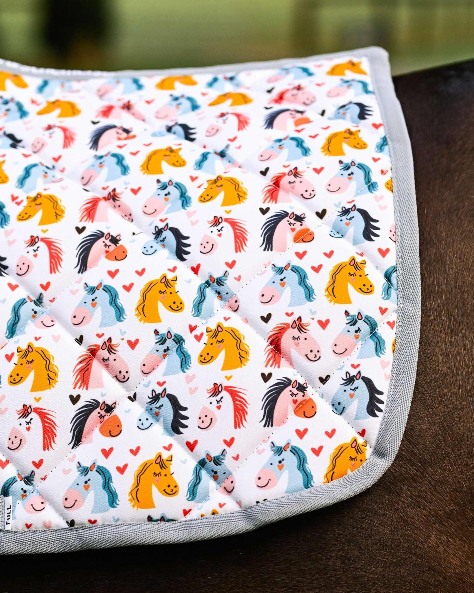 Just Horsing Around youth bundle saddle pad with colorful horse illustrations and hearts on a horse's back