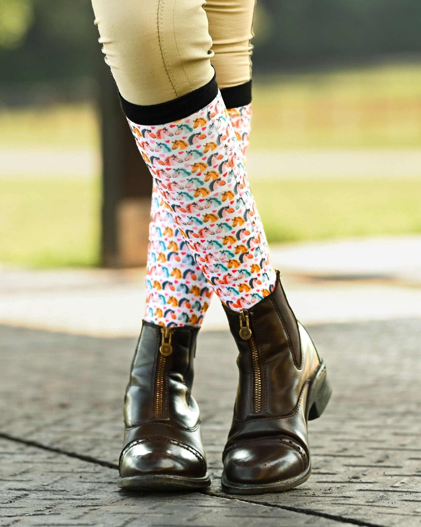 Just Horsing Around youth socks with colorful horse pattern worn with brown riding boots outdoors