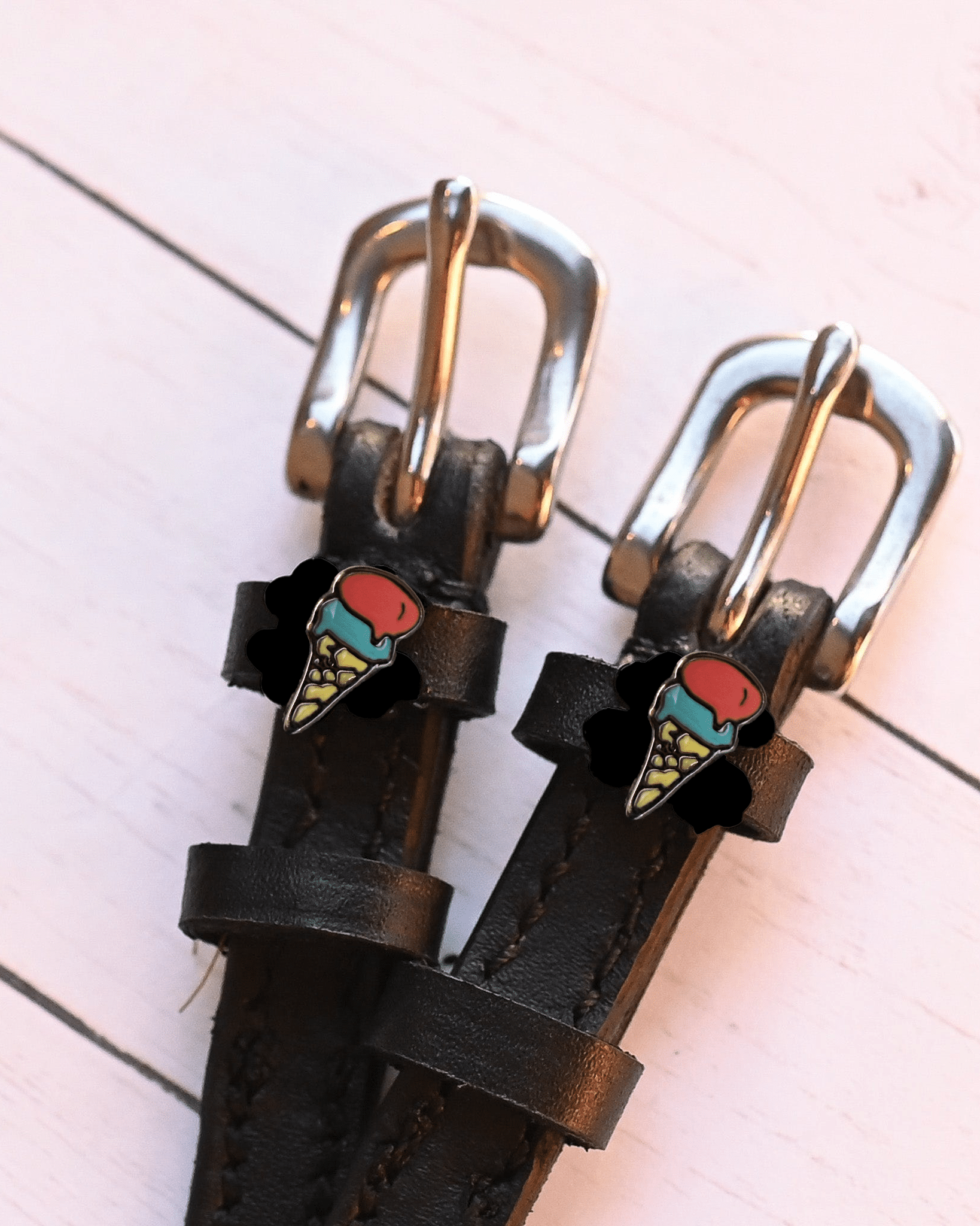 Silver buckles and ice cream cone charms of black leather spur straps on pink wood